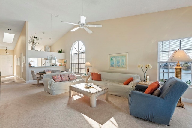 living room featuring a high ceiling, a skylight, light colored carpet, and ceiling fan