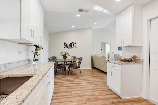 kitchen with white cabinetry, sink, light stone counters, vaulted ceiling, and light wood-type flooring