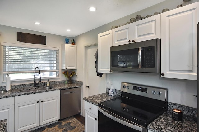 kitchen with white cabinets, stainless steel appliances, dark stone countertops, and sink