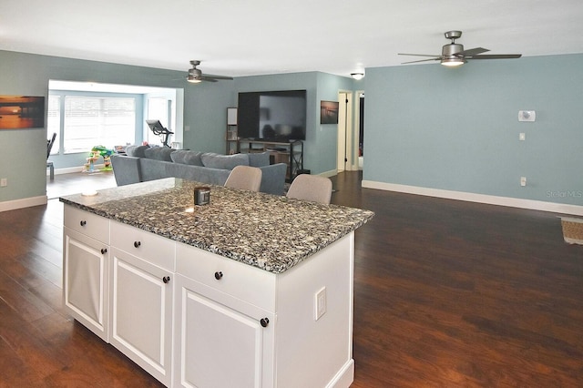 kitchen with white cabinets, a center island, dark hardwood / wood-style flooring, and dark stone counters