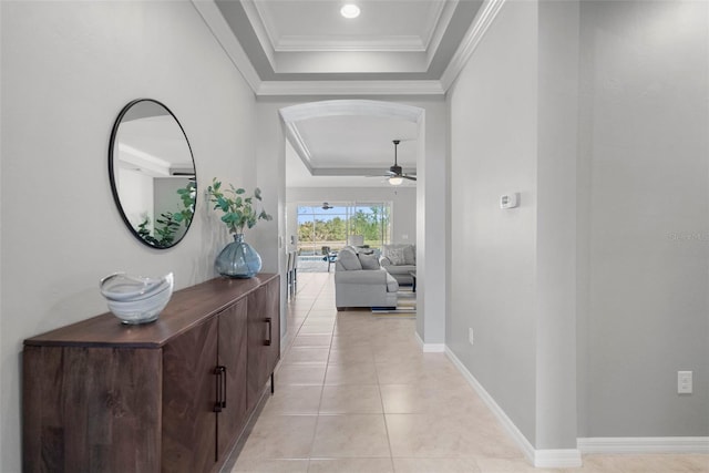 hallway with light tile patterned flooring, crown molding, and a tray ceiling