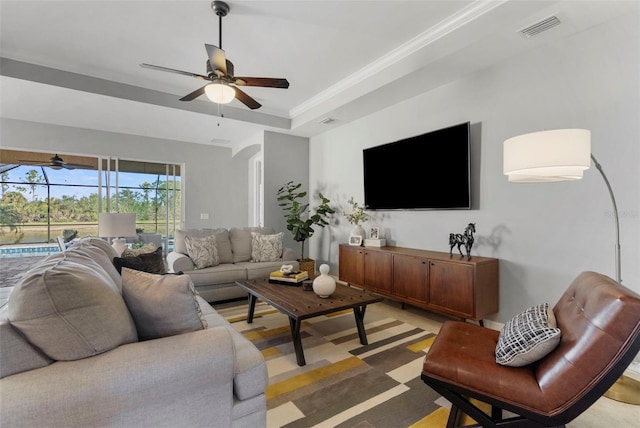 living room featuring ceiling fan, ornamental molding, and a tray ceiling