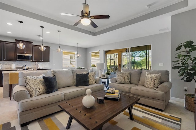 tiled living room featuring ceiling fan with notable chandelier, a raised ceiling, and ornamental molding