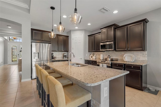 kitchen with sink, stainless steel appliances, an island with sink, decorative light fixtures, and decorative backsplash