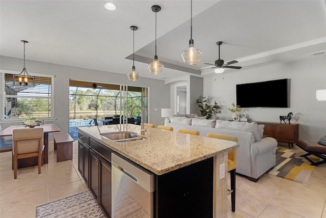 kitchen featuring dishwasher, sink, light stone counters, decorative light fixtures, and a center island with sink