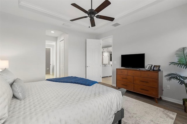 bedroom with hardwood / wood-style flooring, ceiling fan, a raised ceiling, and connected bathroom