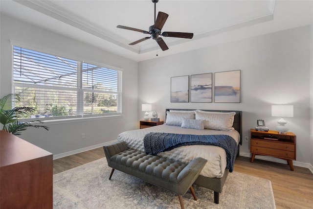 bedroom featuring ceiling fan, light wood-type flooring, and a tray ceiling