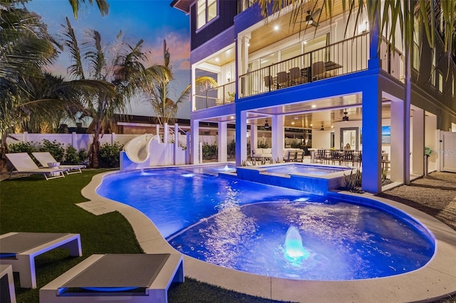 pool at dusk with a patio area, an in ground hot tub, a water slide, and ceiling fan