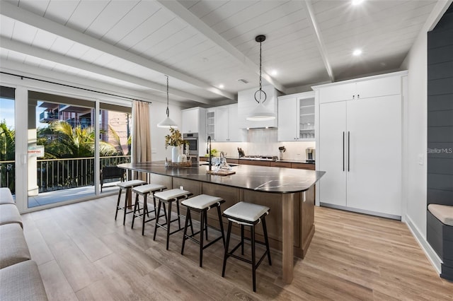 kitchen with pendant lighting, light hardwood / wood-style floors, white cabinetry, and an island with sink