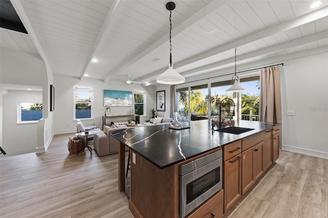 kitchen featuring a kitchen island with sink, sink, decorative light fixtures, light hardwood / wood-style flooring, and stainless steel microwave