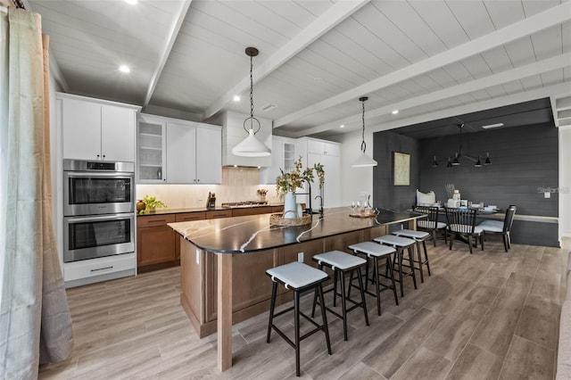 kitchen with appliances with stainless steel finishes, a spacious island, beamed ceiling, white cabinets, and hanging light fixtures