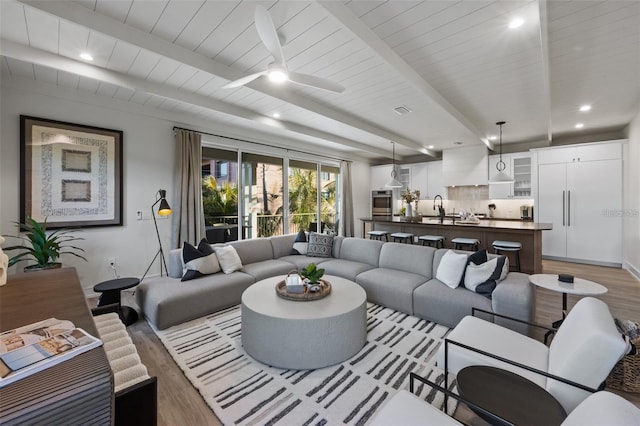 living room featuring ceiling fan, beam ceiling, light wood-type flooring, and sink