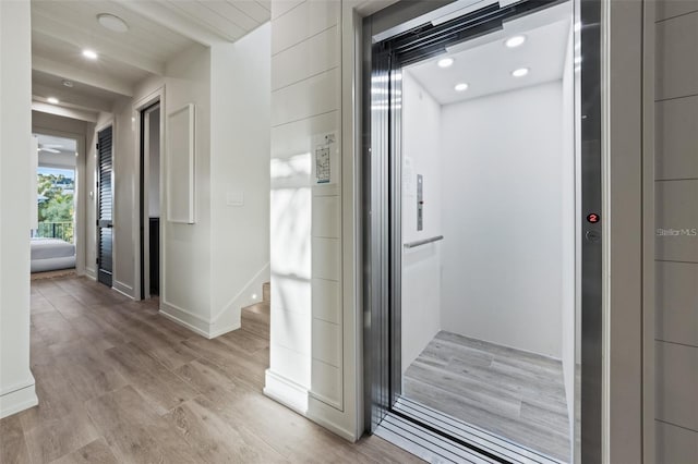 corridor with elevator and light hardwood / wood-style flooring