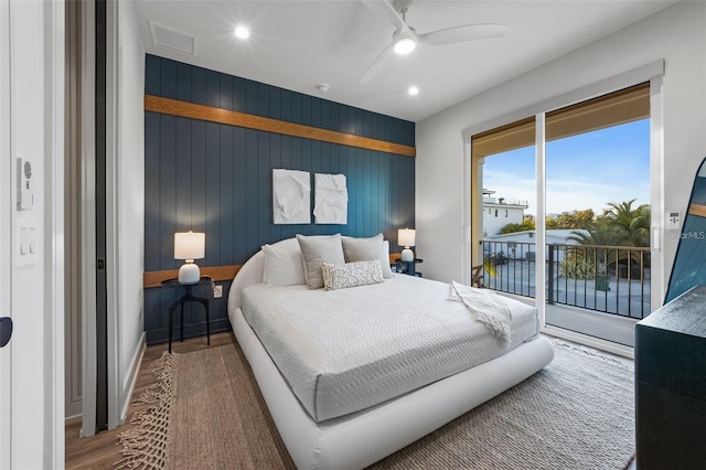 bedroom with access to exterior, hardwood / wood-style floors, ceiling fan, and wood walls