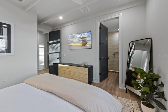 bedroom with hardwood / wood-style floors, ensuite bathroom, and beam ceiling