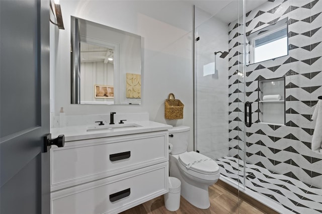 bathroom featuring a tile shower, vanity, toilet, and wood-type flooring