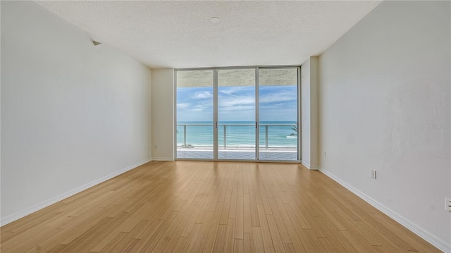 empty room with a textured ceiling, light wood-type flooring, a water view, and a wall of windows