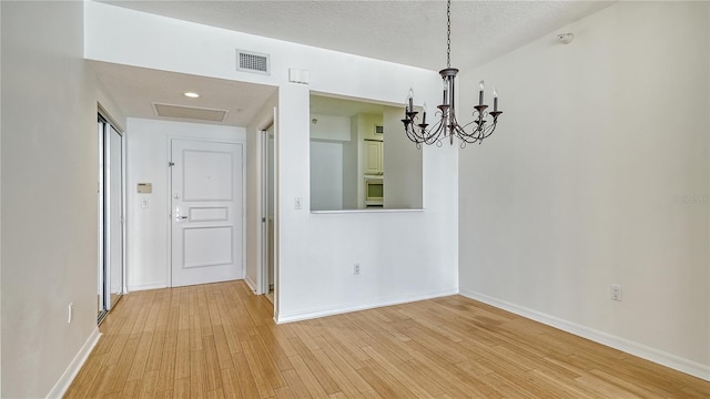 unfurnished dining area with light hardwood / wood-style flooring, a textured ceiling, and a notable chandelier