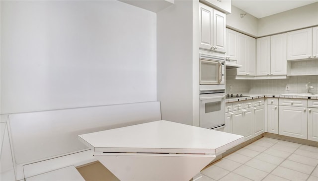 kitchen with white microwave, sink, tasteful backsplash, cooktop, and white cabinetry