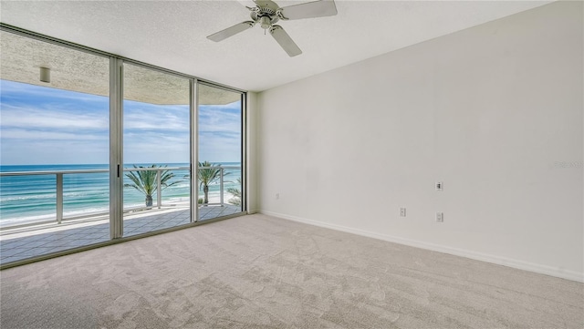 carpeted spare room with ceiling fan, a water view, a beach view, and plenty of natural light