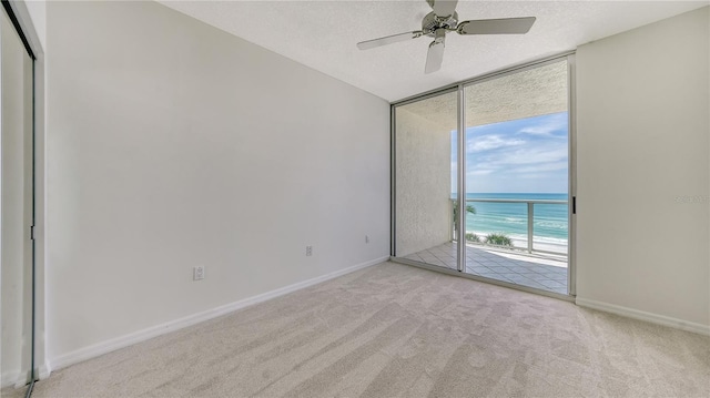 carpeted spare room featuring a textured ceiling, ceiling fan, a water view, and a beach view