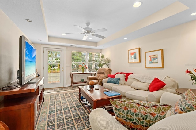 living room with a raised ceiling and ceiling fan