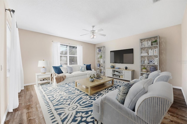 living area with ceiling fan, a textured ceiling, baseboards, and wood finished floors