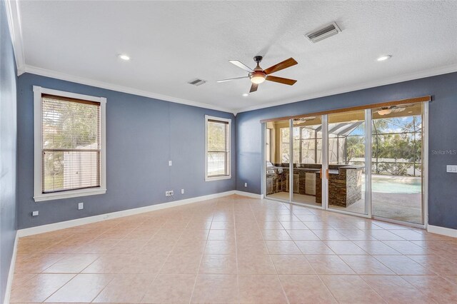 empty room featuring light tile patterned floors, a textured ceiling, a wealth of natural light, and ornamental molding