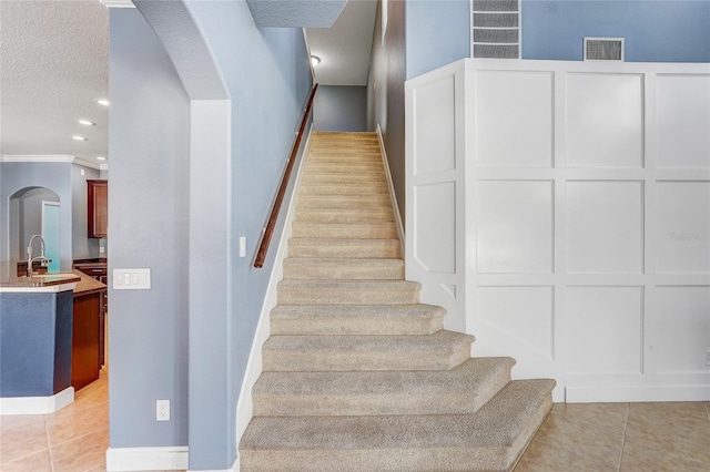 staircase featuring tile patterned flooring, crown molding, sink, and a textured ceiling