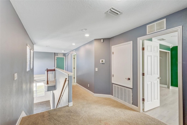 corridor with plenty of natural light, light colored carpet, and a textured ceiling