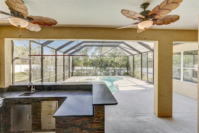 view of patio / terrace featuring a wet bar, glass enclosure, ceiling fan, and exterior kitchen