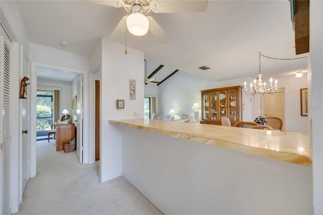 kitchen with ceiling fan with notable chandelier, pendant lighting, light colored carpet, kitchen peninsula, and a textured ceiling