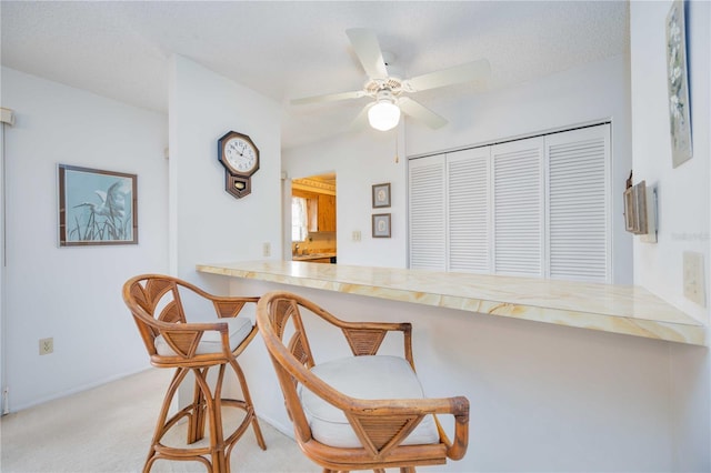 kitchen with a breakfast bar, ceiling fan, a textured ceiling, light carpet, and kitchen peninsula