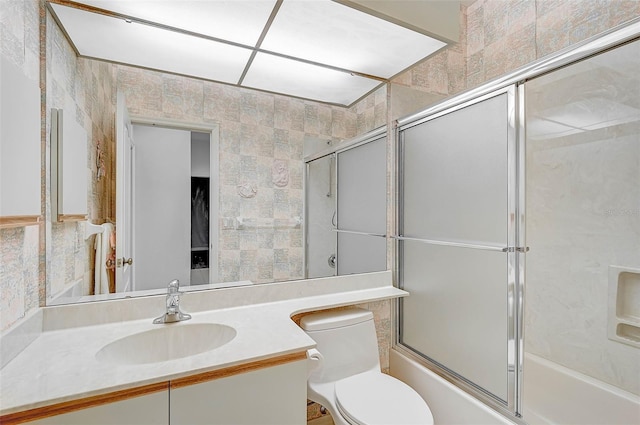 full bathroom featuring vanity, bath / shower combo with glass door, tile walls, and toilet