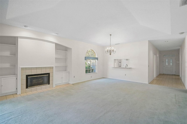 unfurnished living room featuring a textured ceiling, light colored carpet, built in features, an inviting chandelier, and a fireplace