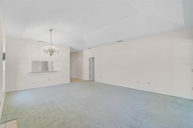 unfurnished living room with a textured ceiling, a raised ceiling, light carpet, and an inviting chandelier