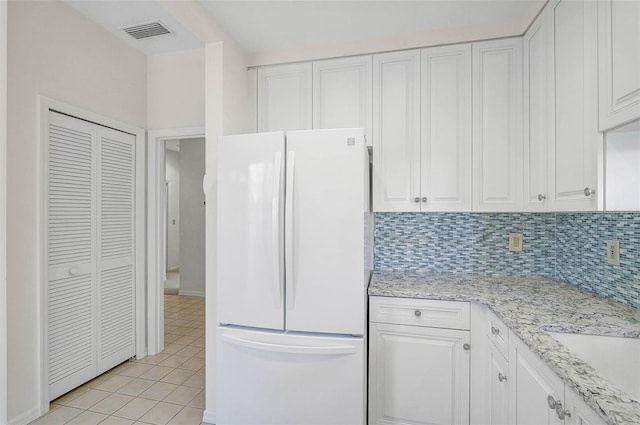 kitchen with white cabinets, white refrigerator, light stone countertops, light tile patterned floors, and tasteful backsplash