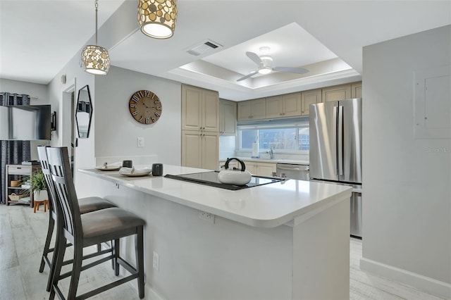 kitchen featuring ceiling fan, stainless steel appliances, kitchen peninsula, a tray ceiling, and a breakfast bar