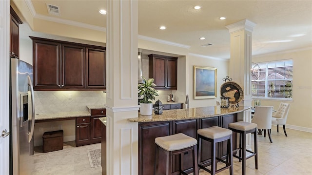 kitchen featuring light stone countertops, backsplash, stainless steel fridge, and ornate columns