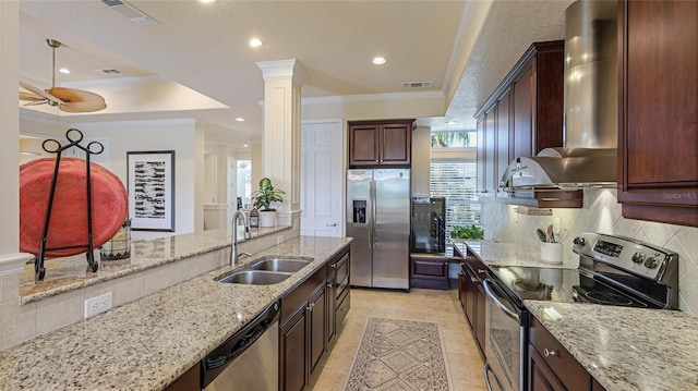 kitchen with light stone countertops, appliances with stainless steel finishes, wall chimney range hood, sink, and a raised ceiling