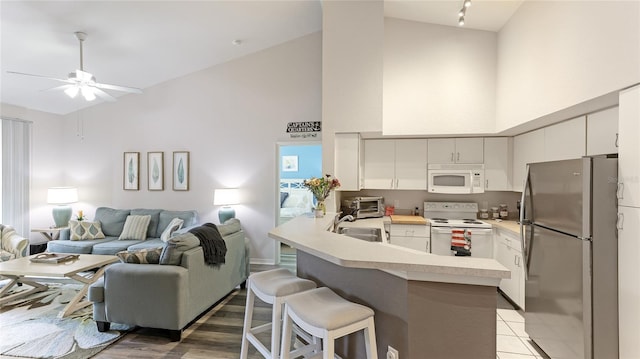 kitchen with a breakfast bar, white appliances, kitchen peninsula, ceiling fan, and white cabinetry