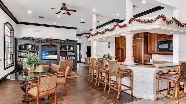 interior space with decorative columns, dark hardwood / wood-style floors, ornamental molding, and ceiling fan