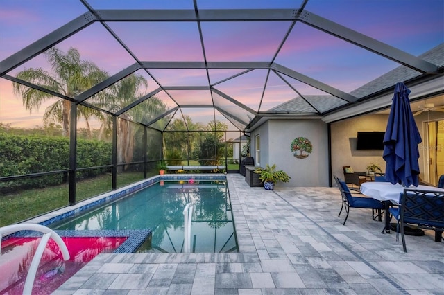 pool at dusk featuring a lanai and a patio