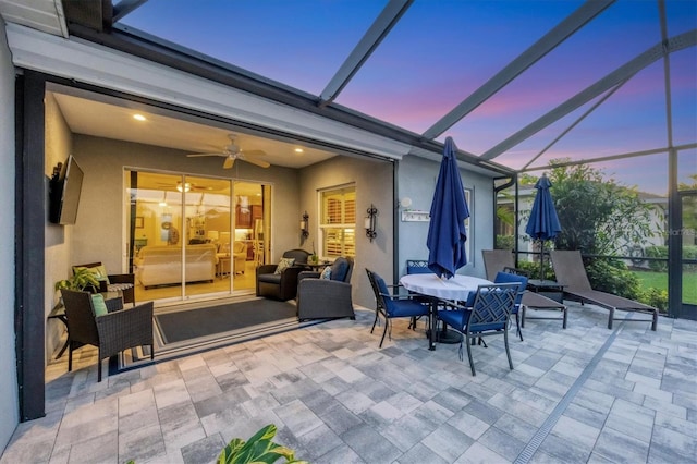 patio terrace at dusk featuring ceiling fan and glass enclosure