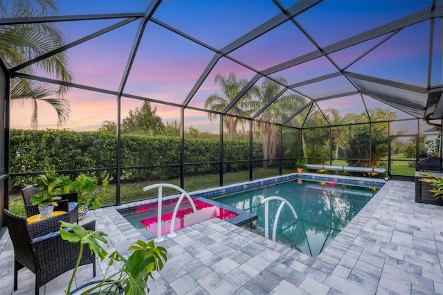 pool at dusk with glass enclosure and a patio