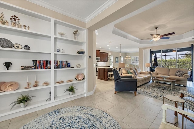 tiled living room with ceiling fan with notable chandelier, a raised ceiling, built in features, and crown molding