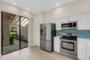 kitchen with tasteful backsplash, light hardwood / wood-style flooring, white cabinets, and stainless steel appliances