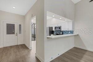 kitchen with kitchen peninsula, appliances with stainless steel finishes, dark hardwood / wood-style flooring, and white cabinetry