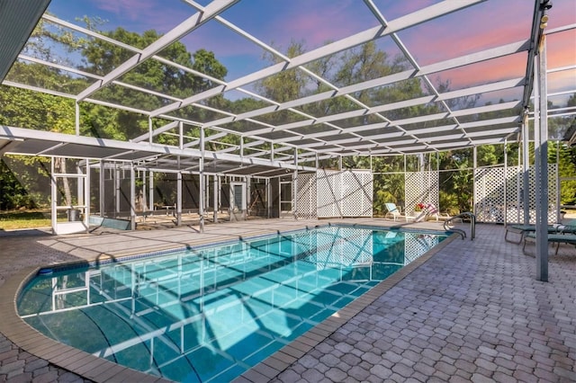 pool at dusk featuring a lanai and a patio