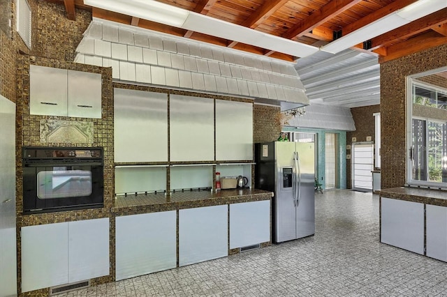 kitchen with white cabinets, oven, stainless steel fridge, and a fireplace